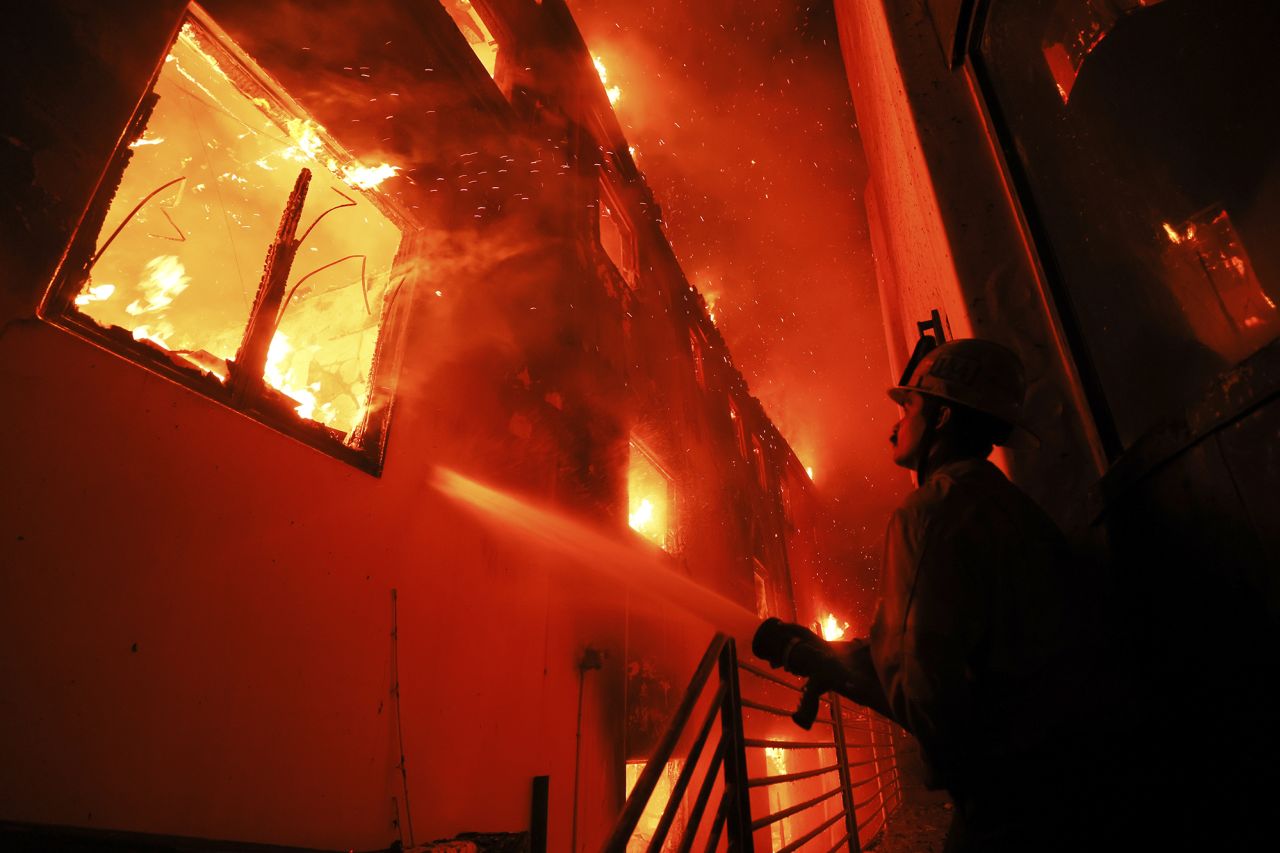 A firefighter works from a deck as the Palisades Fire burns a beach front property on Wednesday, January 8, in Malibu, California.