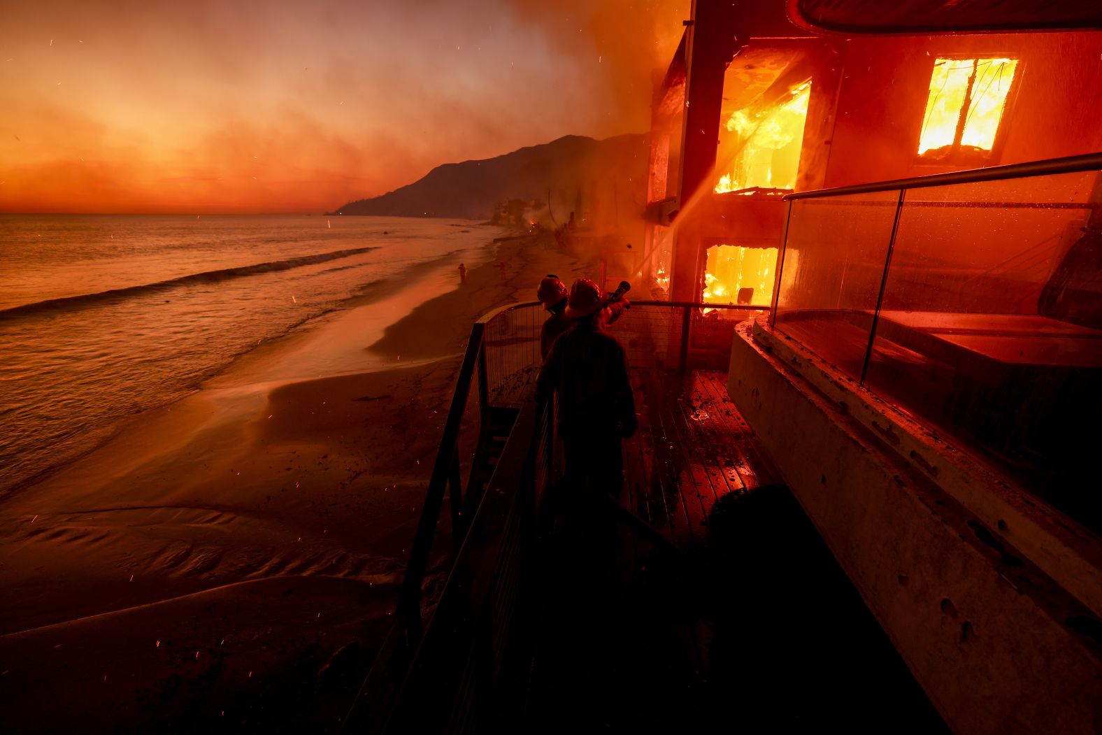 Firefighters work from a deck as the Palisades Fire burns a beachfront property in Malibu.