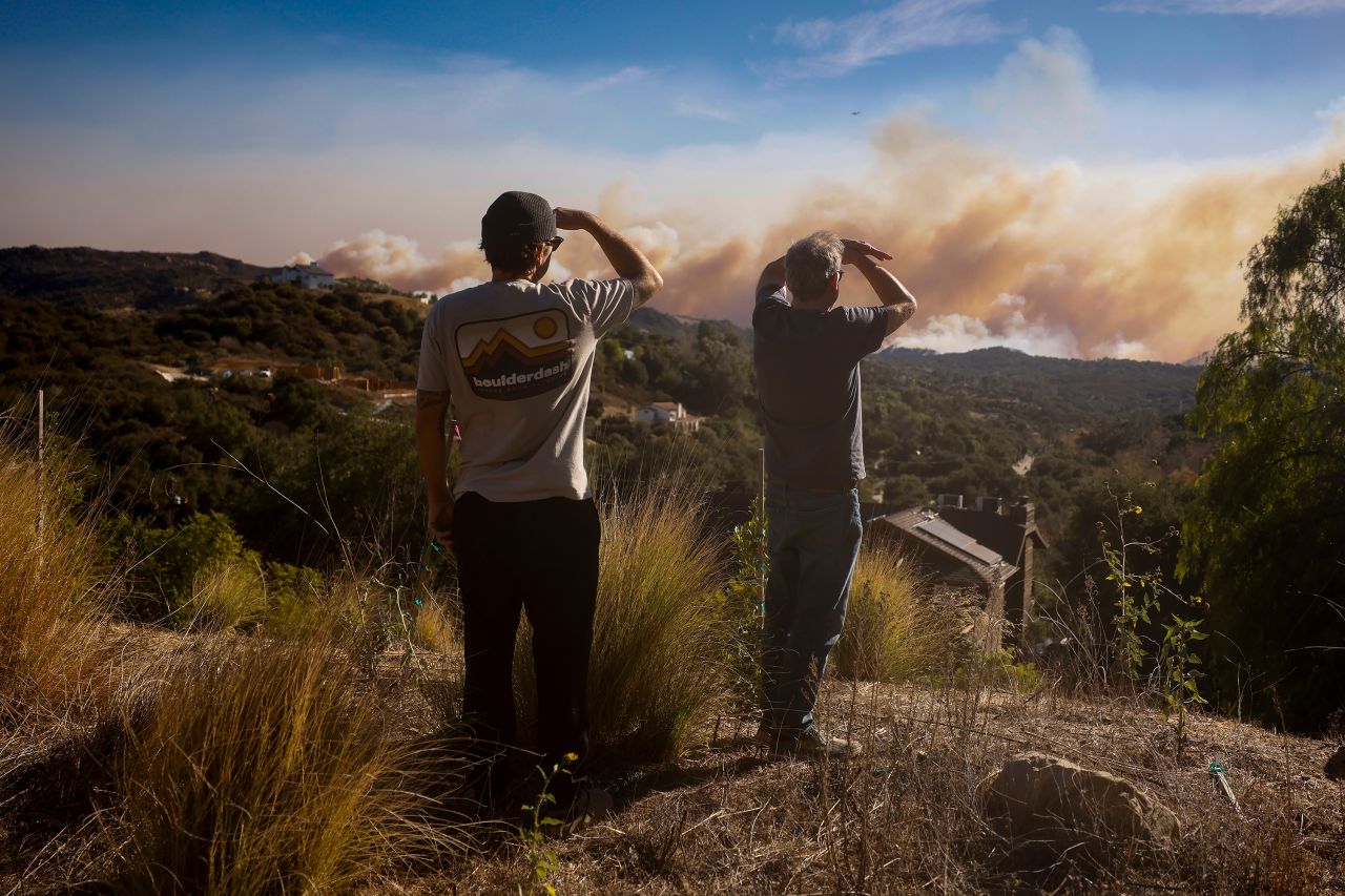 People look on as the Palisades Fire burns in the hills between Pacific Palisades and Malibu on Wednesday, January 8, in Topanga, California.