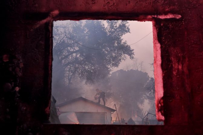 A firefighter is seen through the window of a damaged property while battling the Eaton Fire in Altadena.