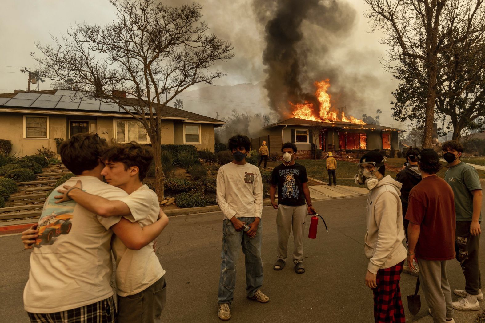 People embrace outside of a burning property in Altadena.