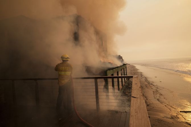 A firefighter protects a beachfront property in Malibu.