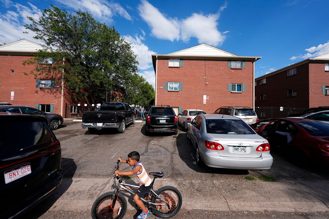 A boy rides his bicycle past apartment buildings as a rally staged by the East Colfax Community Collective is held in the courtyard to address chronic problems in the apartment buildings occupied by people displaced from their home countries in central and South America, on September 3, 2024, in Aurora, Colorado.