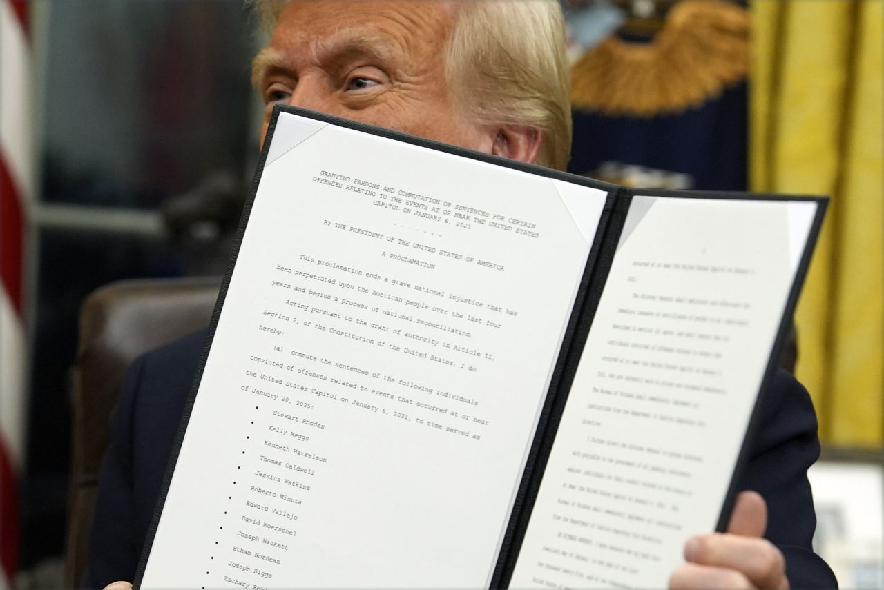 President Donald Trump holds up an executive order commuting sentences for people convicted of January 6 offenses in the Oval Office of the White House, on Monday.