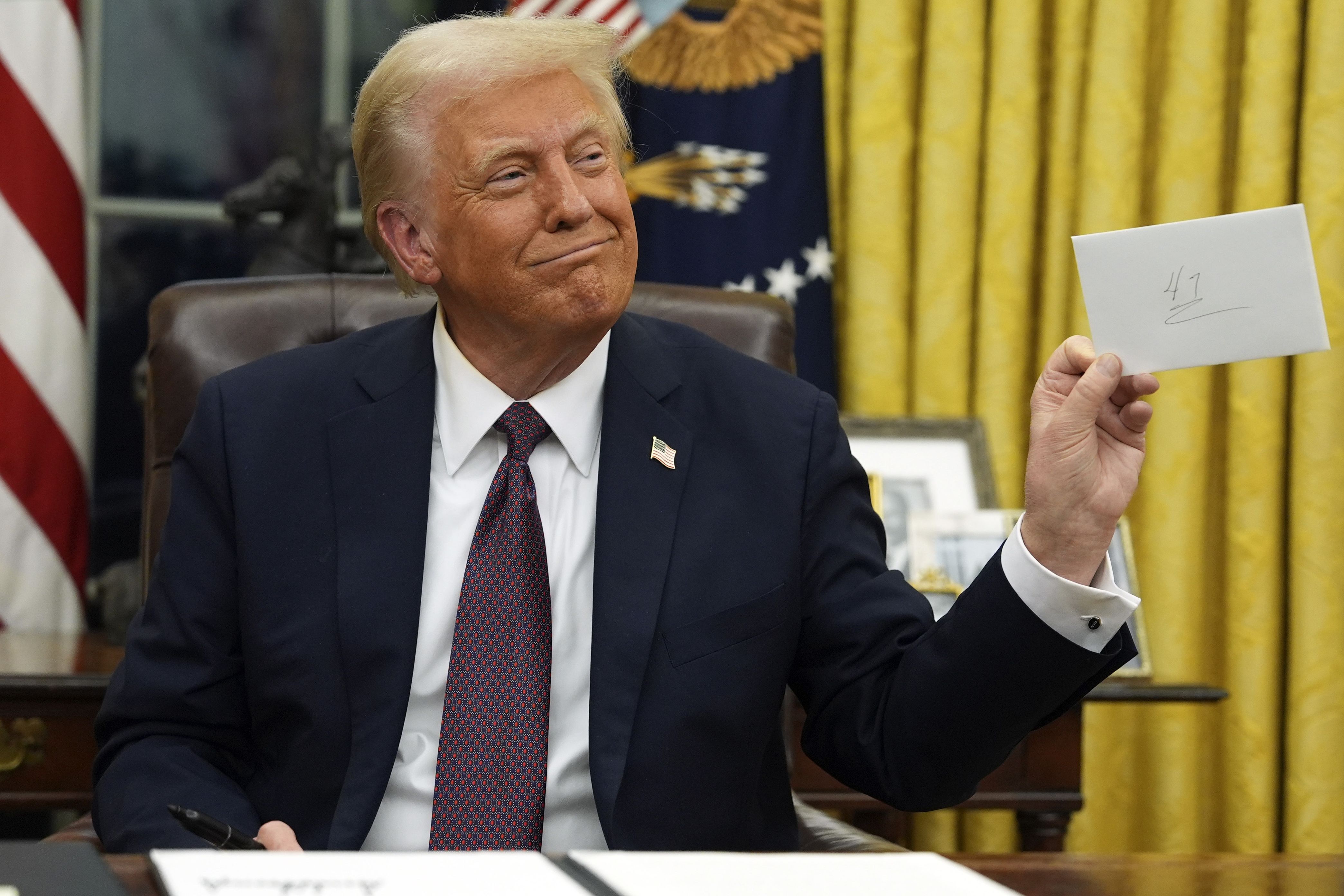 Trump holds up the letter that former President Joe Biden left for him as he signs executive orders in the Oval Office of the White House on Monday.