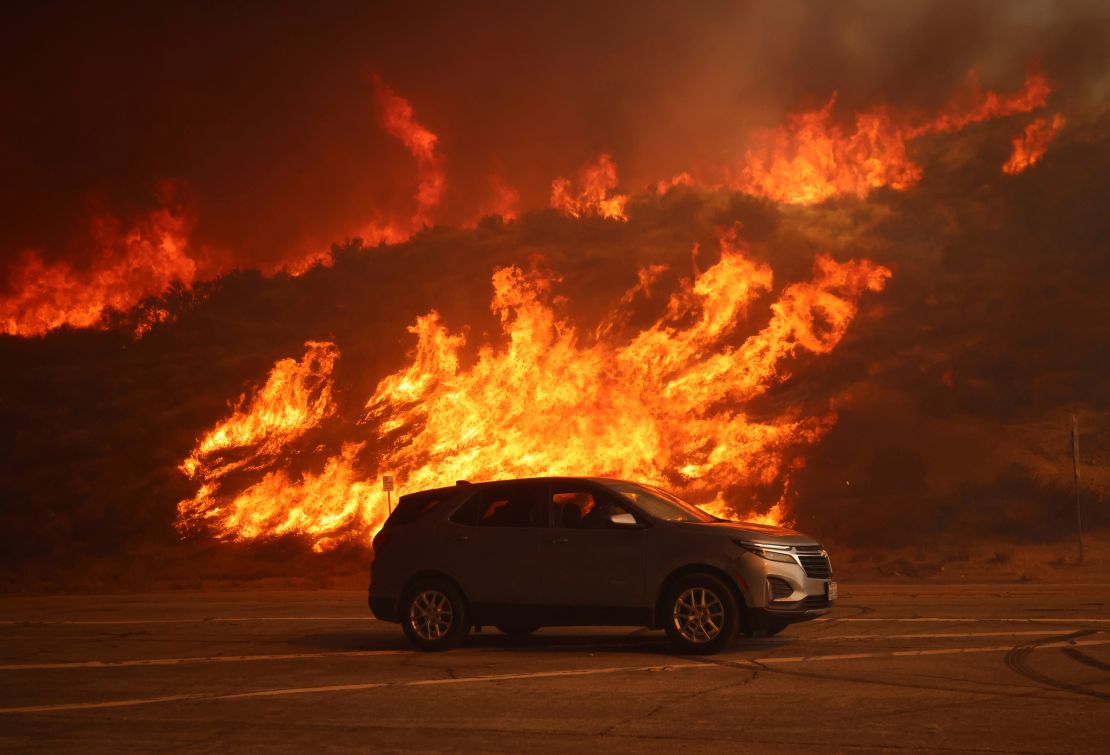 A vehicle rides past a hillside engulfed in flames caused by the Hughes Fire on Wednesday.