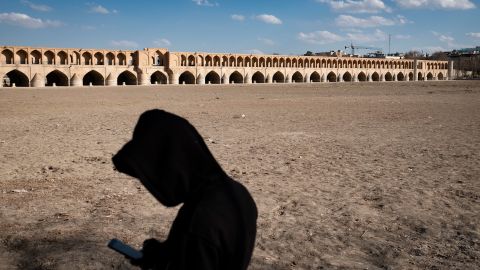 An Iranian man uses his cellphone while standing on the dried-up riverside of the Zayandeh Rud river, with the Si-o-se-pol (33-Bridge) historical bridge visible in the background, in the historic city of Isfahan, Iran, on February 22, 2025. Zayandeh Rud is one of the main tourist attractions of Isfahan, which has completely dried up. Historical bridges such as the 33-Bridge on the river may be damaged due to the subsidence of the Zayandeh Rud riverbed if the drought continues. (Photo by Morteza Nikoubazl/NurPhoto via AP)