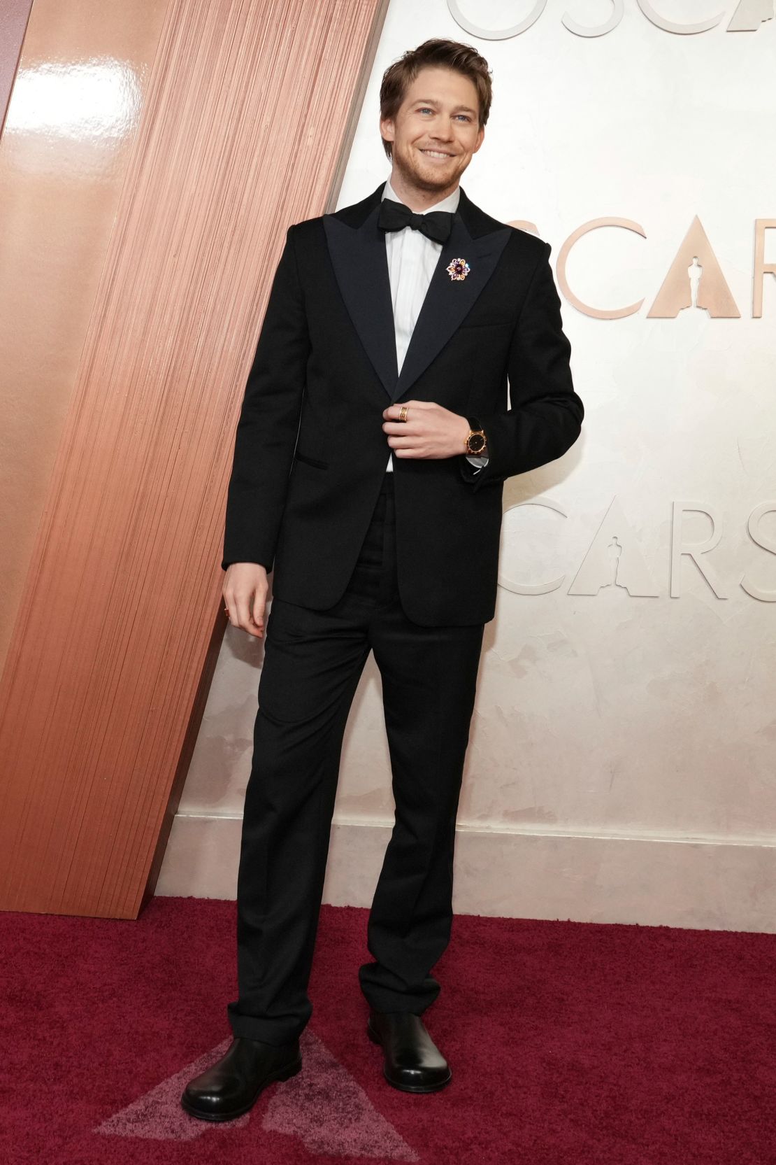 Joe Alwyn kept it classy in a black suit accessorized with Bulgari jewelry – a multicolored brooch paired with a yellow gold watch and rings.