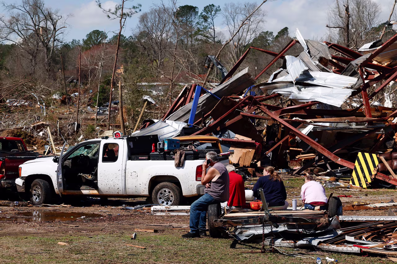 Friends and family members take a break as they search for belongings in the damage after a tornado passed through the area, Sunday, in Plantersville, Alabama.