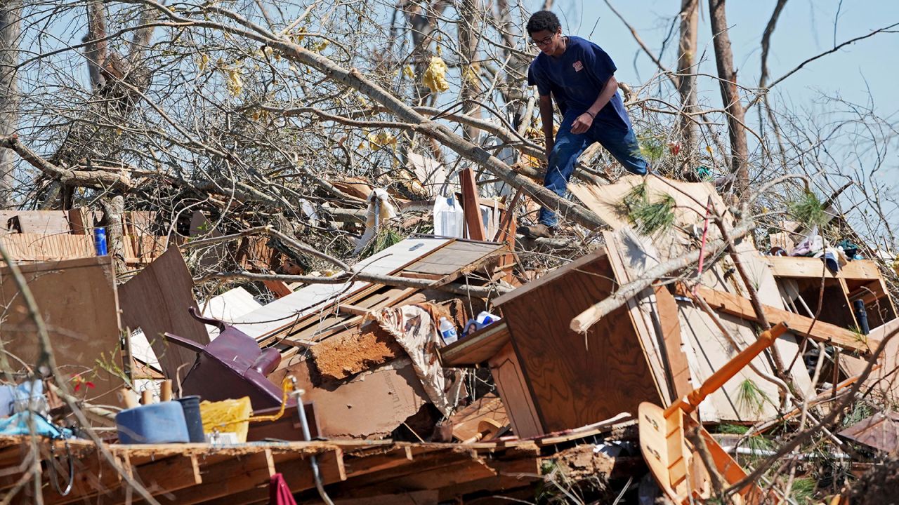 Family friend Trey Bridges, 16, climbs a mountain of tornado debris to help the Blansett family recover items not destroyed by Saturday's tornado, Sunday, March 16, 2025, in Tylertown, Miss. (AP Photo/Rogelio V. Solis)