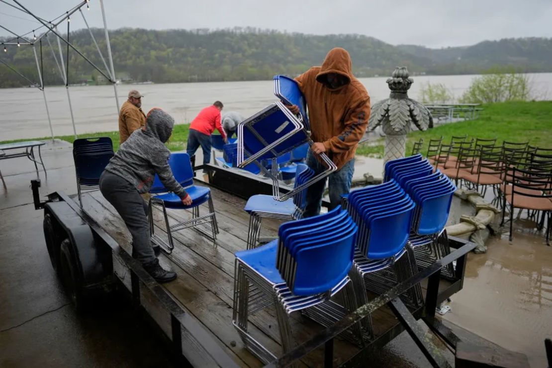 La gerente de Drew’s on the River Sports Bar and Grill, Carrie Haines, a la izquierda, y Dave Schmidt, hijo del propietario Ron Schmidt, a la derecha, cargan sillas en un remolque bajo la lluvia para trasladarlas a un terreno más alto mientras el río Ohio crece detrás de ellos, en Cincinnati, Ohio, el viernes.