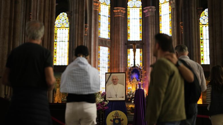 People stand next to a photograph of Pope Francis placed at Saint Anthony Catholic church in Istanbul, Turkey, Monday, April 21, 2025. (AP Photo/Khalil Hamra)