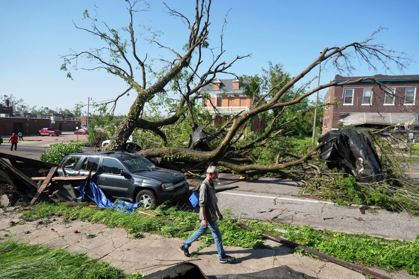 A person walks past a large tree blocking a road after a severe storm moved through in St. Louis, on Friday.