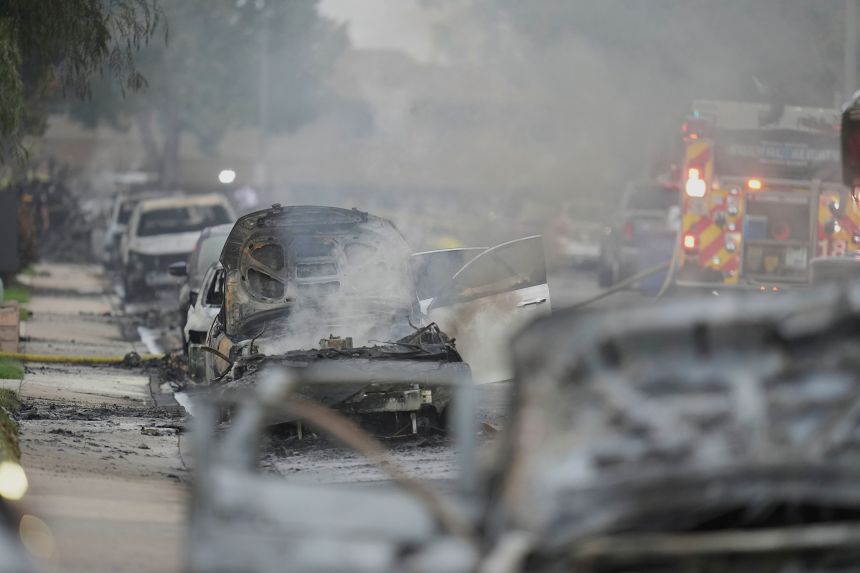 Vehicles are damaged when the authorities work the scene in which a small plane crashed into a neighborhood in San Diego early Thursday.
