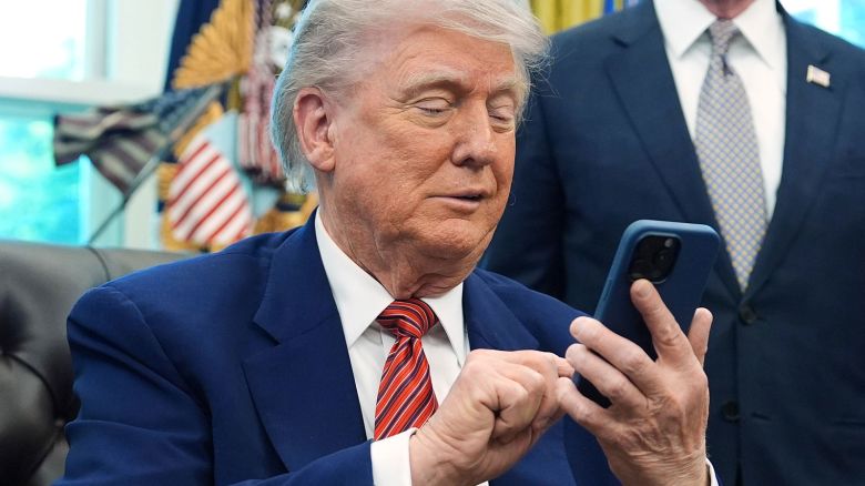 President Donald Trump silences his mobile phone which rang two times as he was speaking to reporters after signing executive orders regarding nuclear energy in the Oval Office of the White House, Friday, May 23, 2025, in Washington. (AP Photo/Evan Vucci)