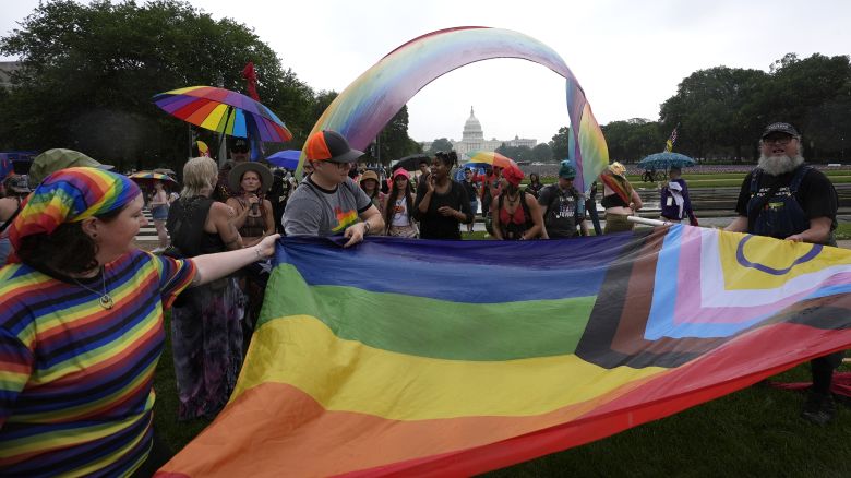 People roll up a wet flag during the World Pride Rally and March with the U.S. Capitol building in the background, Sunday, June 8, 2025, on the National Mall in Washington.