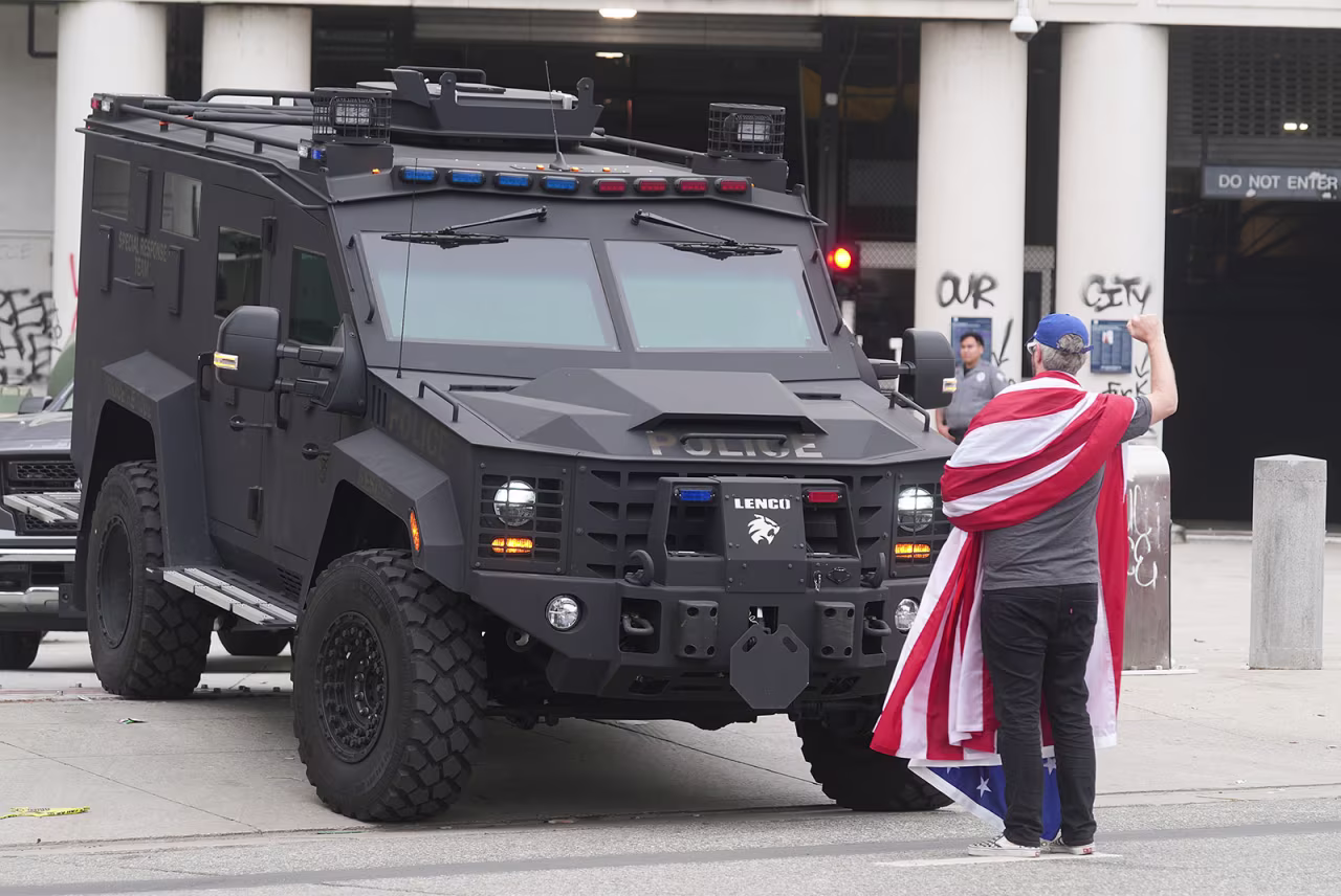 A lone demonstrator draped in a U.S. flag stands outside of the Metropolitan Detention Center in Los Angeles on Thursday.