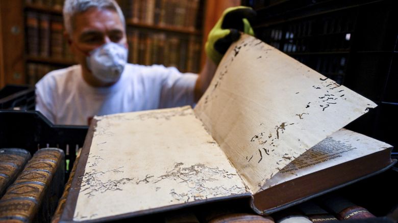 In this photo provided by Pannonhalma Archabbey, a restorer shows an old book with holes in its pages due to a drugstore beetle infestation, at the Pannonhalma Archabbey's library in Pannonhalma, Hungary, Thursday, July 3, 2025, as a beetle infestation threatens its ancient collection.