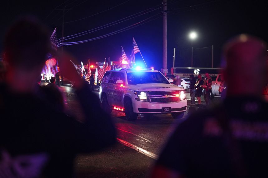 People salute as a York County sheriff vehicle drives past during a procession Wednesday in Spring Grove, Pennsylvania, after five police officers were shot, leaving three dead.
