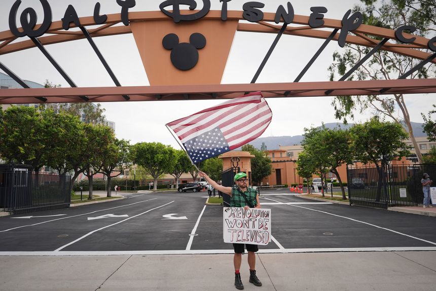 Eddy Patino holds a sign and waves a US flag at a demonstration in response to the suspension of Jimmy Kimmel's late-night show outside of The Walt Disney Studios on Thursday, in Burbank, California.