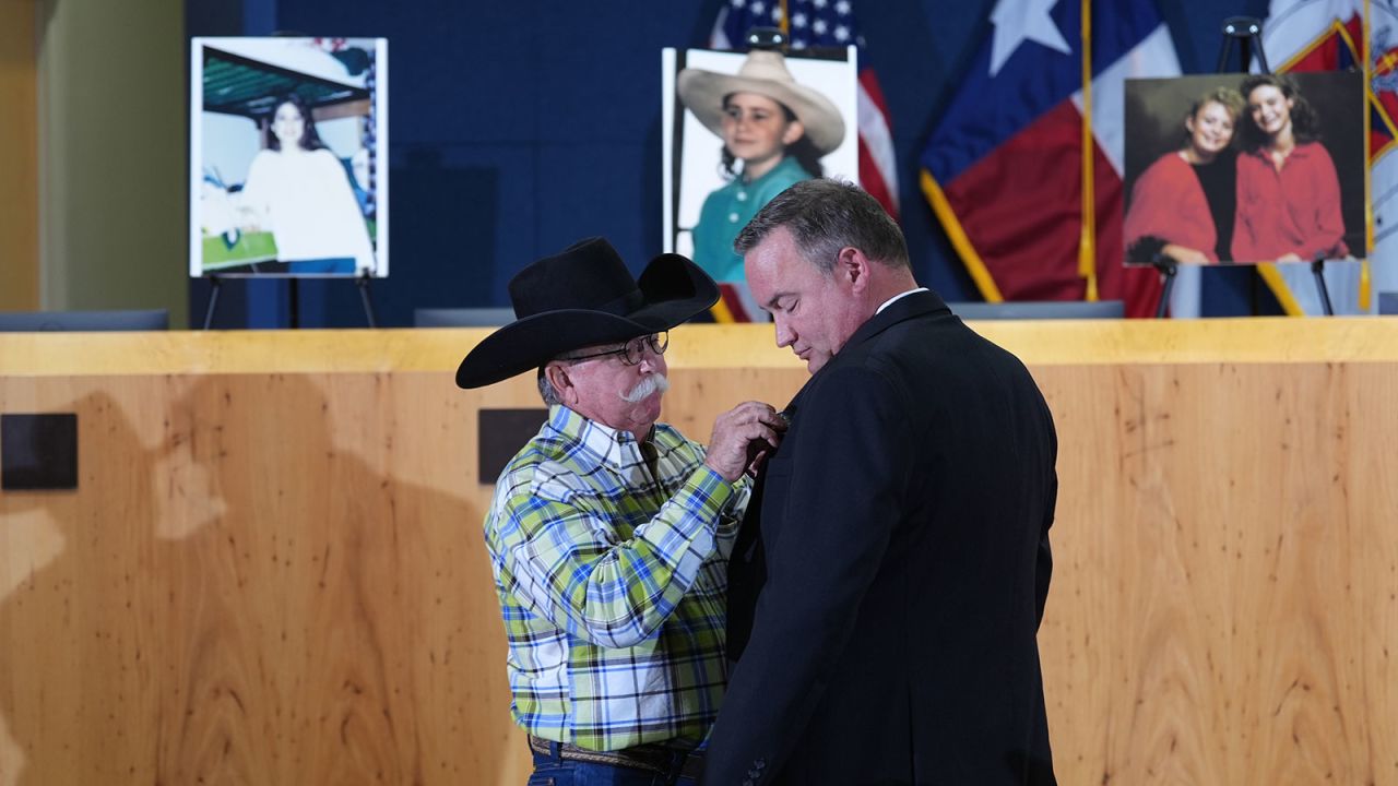 Austin Police Cold Case Detective Daniel Jackson, right, is given a pin that says "We Will Not Forget" by Bob Ayers, father of victim Amy Ayers, during a news conference regarding a breakthrough in the 1991 I Can't Believe It's Yogurt murder case, on September 29, in Austin.