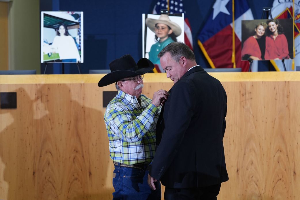 Bob Ayers, the father of Amy Ayers, a victim of the Austin, Texas, yogurt shop murders in 1991, places a "We Will Not Forget" pin on Austin Police Detective Dan Jackson at a news conference on September 29. Amy's picture is above them, alongside photos of the other three victims.