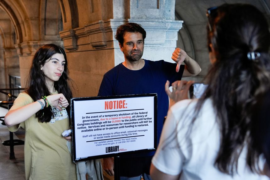 People take photos with a sign announcing that the Library of Congress is closed, on the first day of a partial government shutdown, Wednesday, Oct. 1, 2025, in Washington. (AP Photo/Julia Demaree Nikhinson)