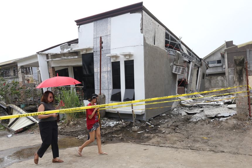 İki kadın, 10 Ekim'de Filipinler'in güneyindeki Davao şehrinde meydana gelen şiddetli depremin ardından hasar gören bir evin önünden geçiyor.