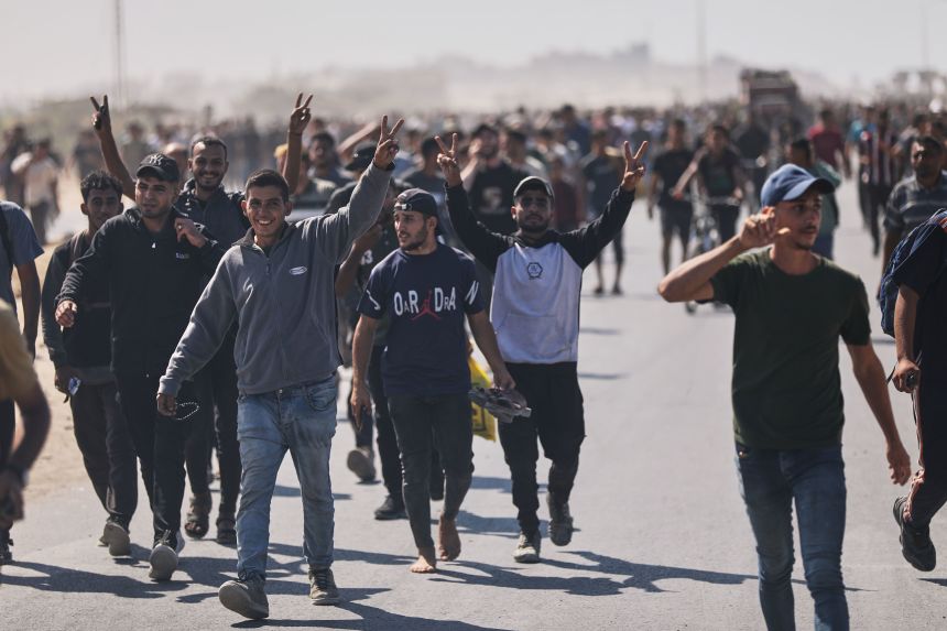 Displaced Palestinians wave to the camera as they walk along the coastal road in the direction of Gaza City on Friday, October 10, 2025.