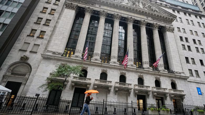 A woman with an umbrella passes the New York Stock Exchange, on Oct. 13, 2025.