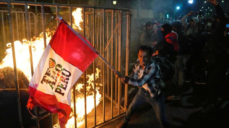 A demonstrator waves a Peruvian flag as a cardboard doll burns in front of Congress during a protest against new President Jose Jeri in Lima, Peru on October 15, 2025.