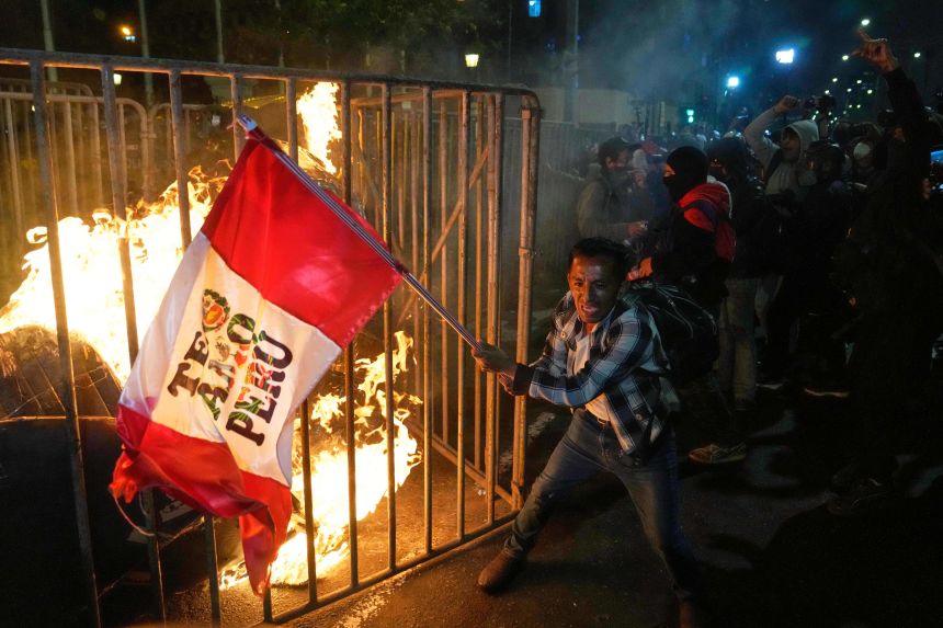 A demonstrator waves a flag as a cardboard doll burns in front of Congress during a protest against new President Jose Jeri in Lima, Peru on October 15, 2025.