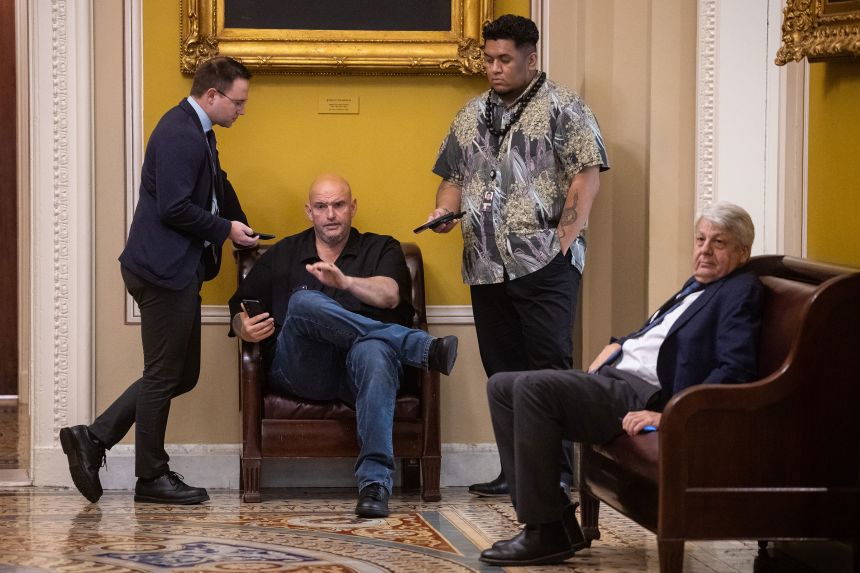 Sen. John Fetterman is seen with reporters and an aide as he sits on a bench near the Senate chamber at the US Capitol on October 30, 2025.