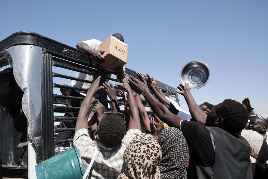 Sudanese families displaced from el-Fasher reach out as aid workers distribute food at the newly established El-Afadh camp in Al Dabbah, in Sudan's Northern State, on November 16.