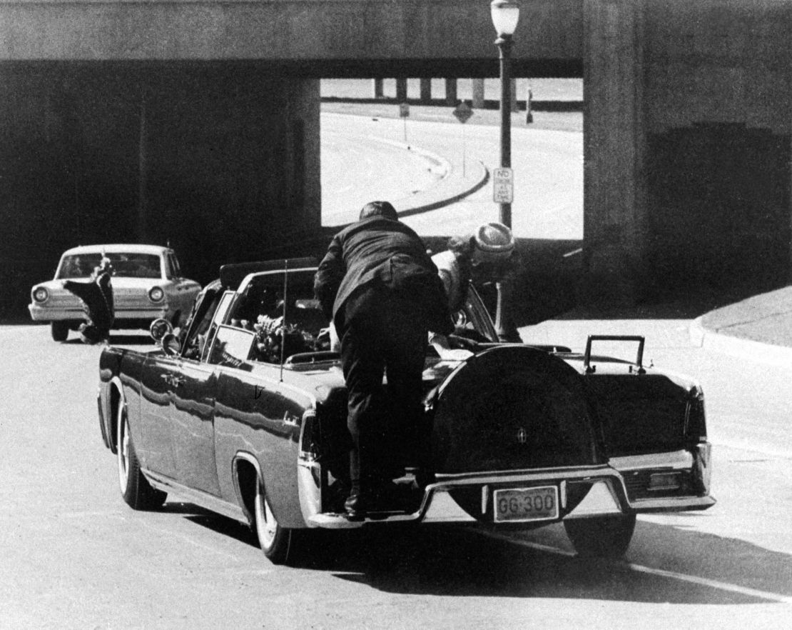 President John F. Kennedy slumps down after being fatally shot in the presidential limousine as it speeds toward the hospital in Dallas on November 22, 1963, with Jacqueline Kennedy leaning over him.