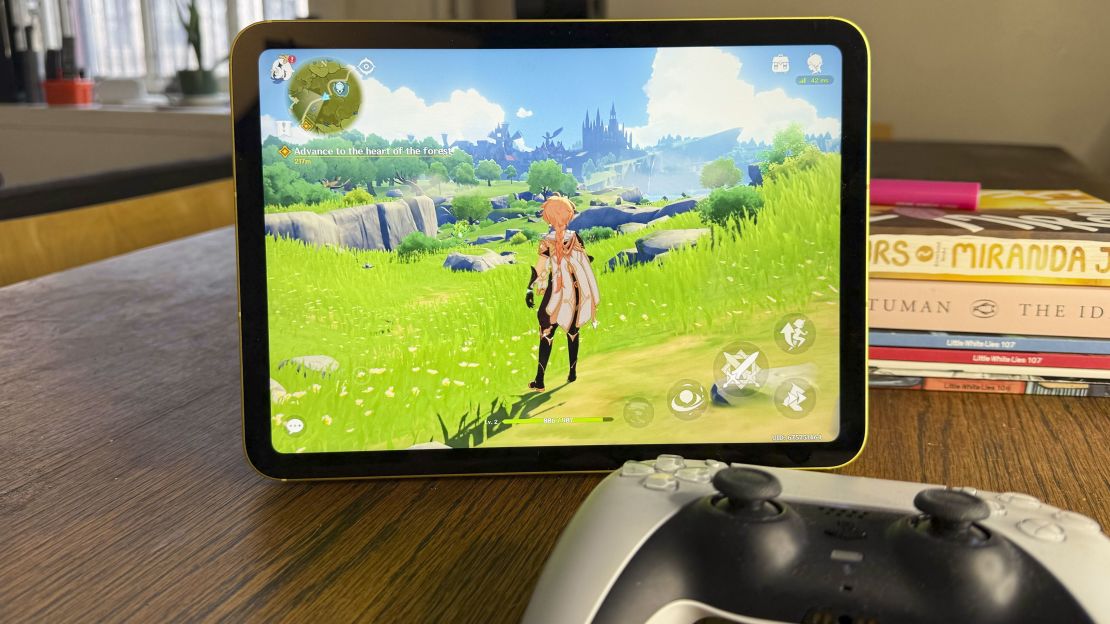 The iPad 11 shows a bright video game, a playstation controller is in the foreground