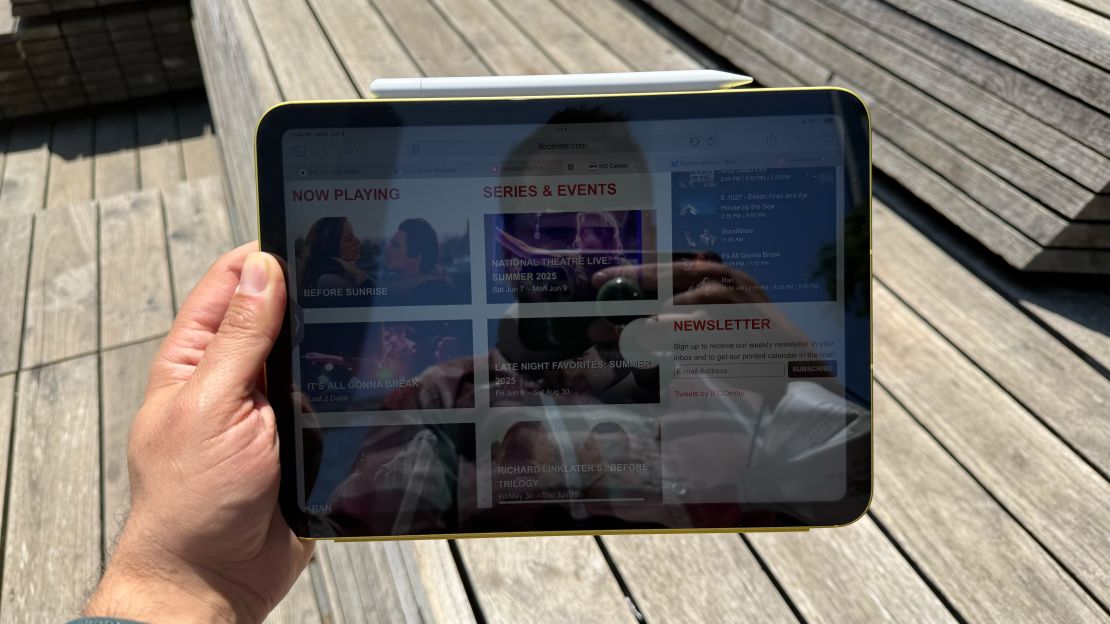 A hand holds an iPad 11 which is showing a slightly visible web page for a movie theater, but the image isn't bright