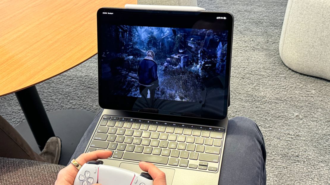 Resident Evil 4 is playing on an iPad Pro, which is on the Magic Keyboard stand while the gamer holds a PS5 controller.