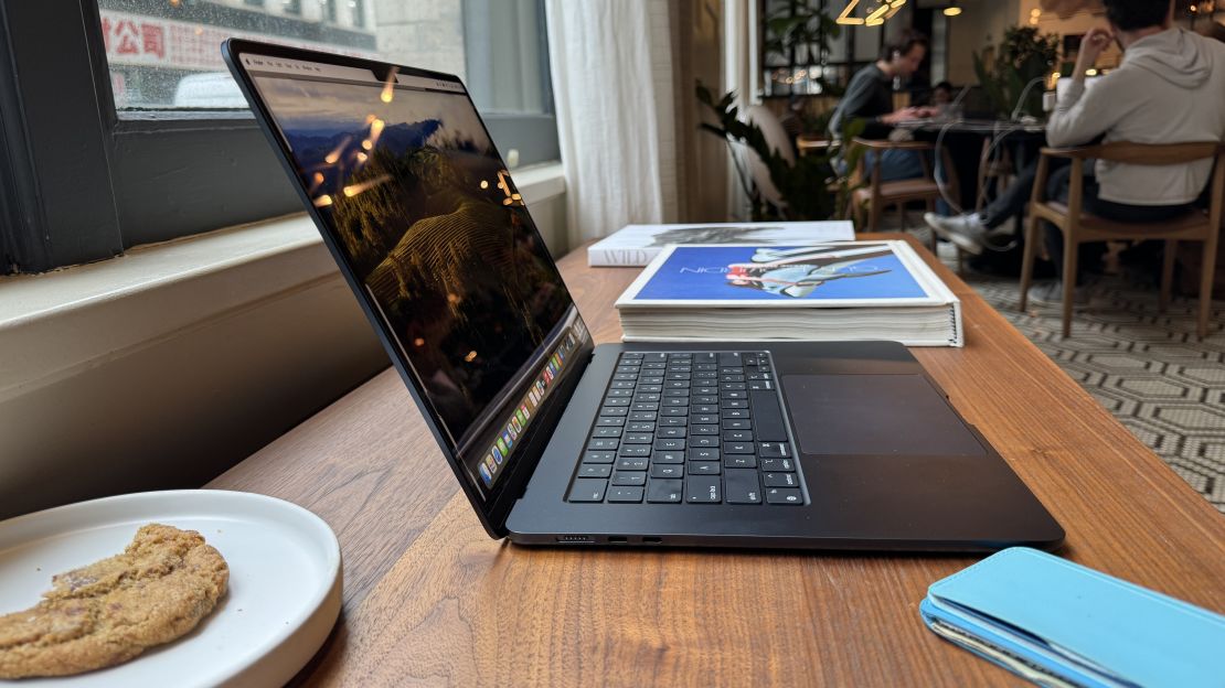 The 15-inch Apple MacBook Air M3 seen from the side with display open, with a coffee shop in the background.