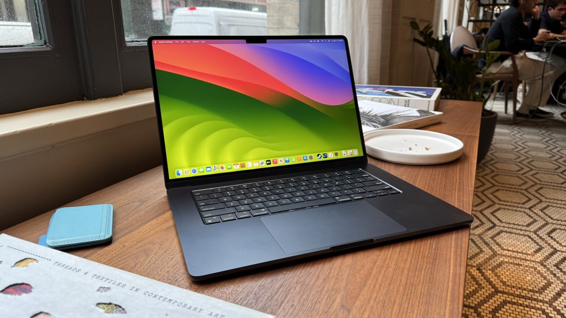 The 15-inch Midnight Blue MacBook Air with M3 has an empty desktop, and has a blue wallet on its left and an empty plate on its right. 