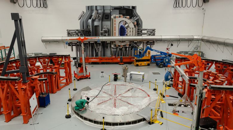 A person works on the cryostat base of the fusion reactor inside the tokamak hall at Commonwealth Fusion Systems in Devens, Massachusetts, on April 10. A full-sized image of the tokamak is superimposed onto the wall.<br /><br /><br /><br /><br /><br /><br /><br /><br /><br /><br /><br /><br /><br />