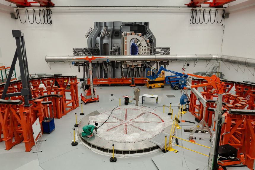 A person works on the cryostat base of the fusion reactor inside the tokamak hall at Commonwealth Fusion Systems in Devens, Massachusetts, on April 10. A full-sized image of the tokamak is superimposed onto the wall.