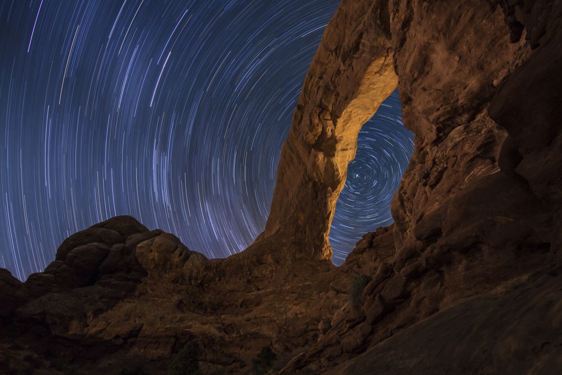 A long-exposure photograph showing star trails in the night sky over Arches National Park, Utah, a Dark Sky reserve.