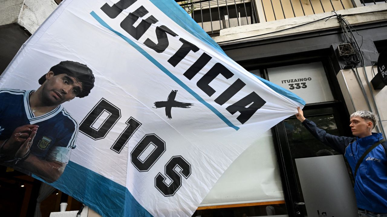 A fan holds a flag with his image of late Diego Maradona in front of the San Isidro court ahead of the trial for the death of late Argentine football legend Diego Maradona in San Isidro, Buenos Aires province, Argentina on March 11, 2025. Four years after Diego Maradona's death, the trial of seven health professionals begins this Tuesday in Argentina to determine their responsibilities in the death of the soccer legend. (Photo by Luis ROBAYO / AFP) (Photo by LUIS ROBAYO/AFP via Getty Images)          
