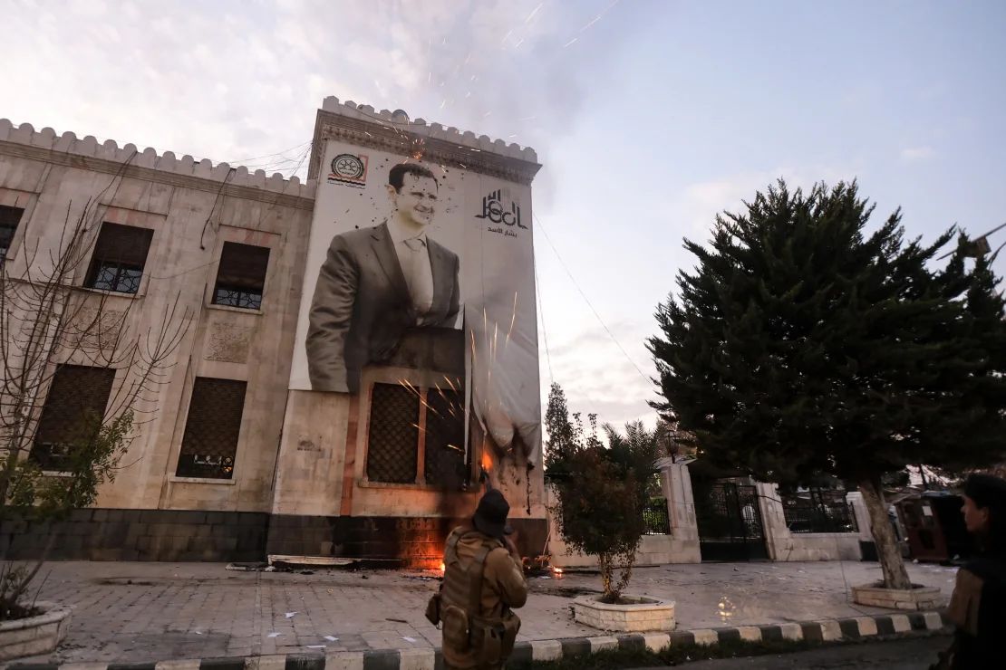 Un combatiente rebelde dispara a una pancarta con la imagen del presidente de Siria, Bashar al-Assad, colgada en la fachada de un edificio municipal, en Hama, Siria, el 5 de diciembre.