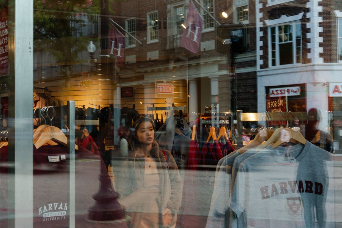School flags are reflected Thursday in a storefront on Harvard Square.