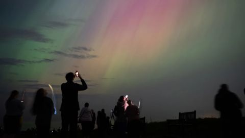 Personas observan auroras boreales sobre el faro de St. Mary en Whitley Bay, en la costa de Inglaterra, en mayo de 2024.