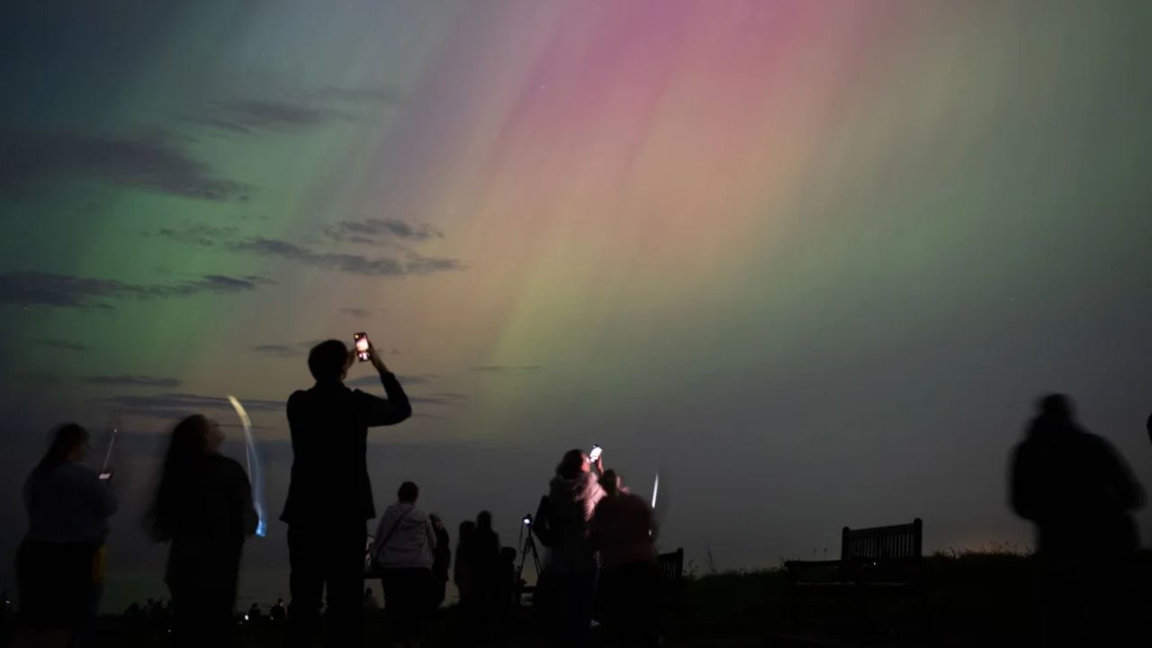 Personas observan auroras boreales sobre el faro de St. Mary en Whitley Bay, en la costa de Inglaterra, en mayo de 2024.