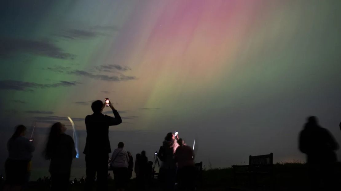 Personas observan auroras boreales sobre el faro de St. Mary en Whitley Bay, en la costa de Inglaterra, en mayo de 2024.