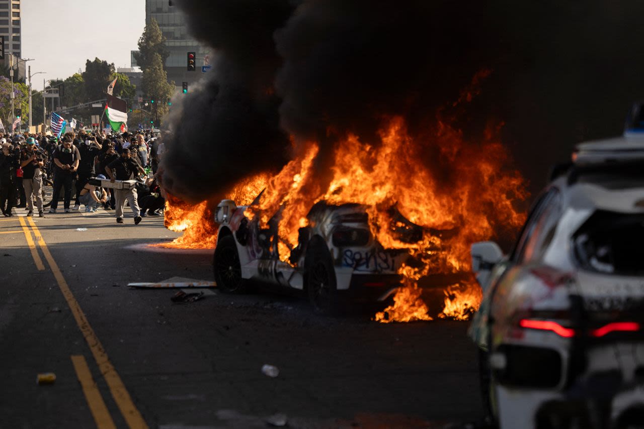 Autos Waymo son incendiados mientras los manifestantes se enfrentan con la policía cerca del edificio federal durante una protesta en respuesta a las operaciones federales de inmigración en Los Ángeles el domingo.